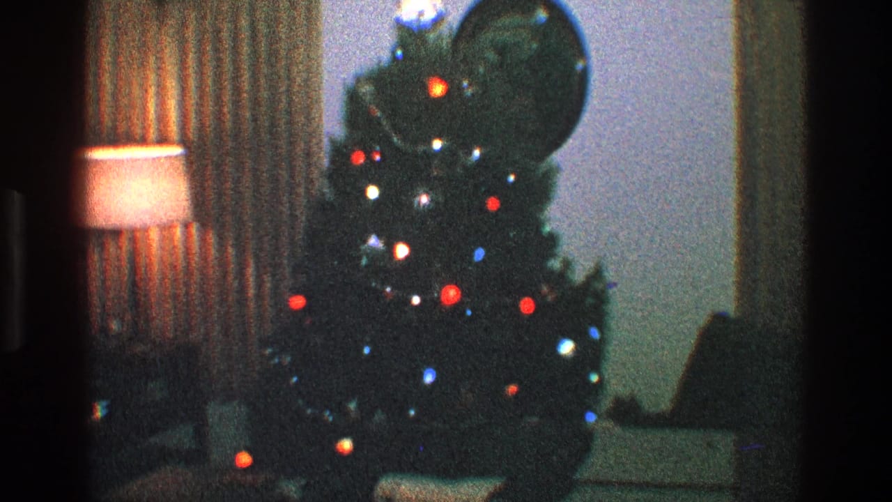 Lit Christmas tree beside a warm lamp, patterned curtains, and round wall mirror.