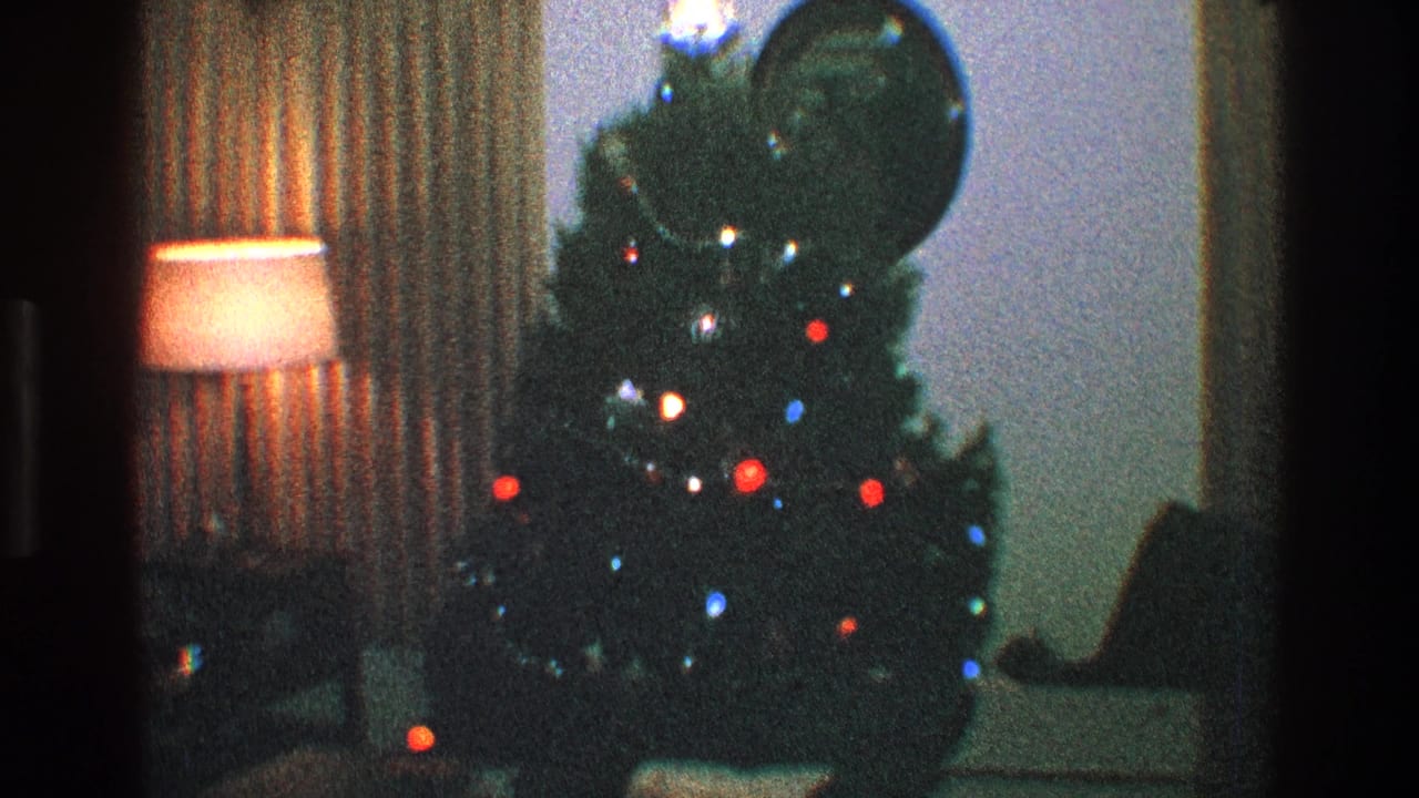 Christmas tree with colored lights near a lamp, curtains, and round wall mirror.