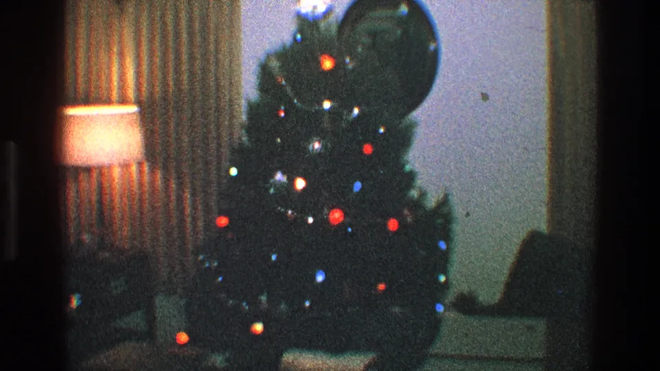 1968 Toledo 8mm frame showing the Christmas tree from a similar angle with colored lights, a shaded lamp, curtains, and wall mirror.