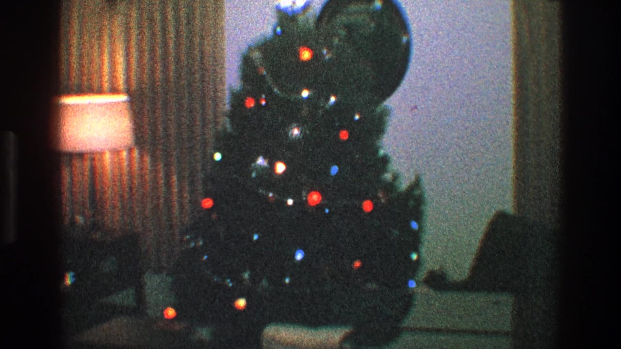 Decorated Christmas tree beside a glowing lamp and striped curtains in a dim living room.