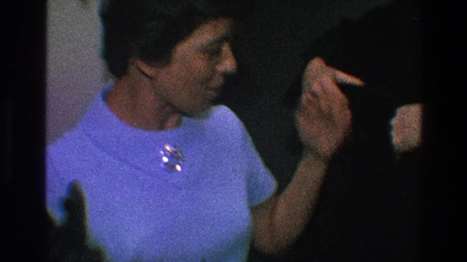 The woman gestures while talking with a man in a dark coat, captured in a brief 1968 Toledo Christmas interior home-movie moment.