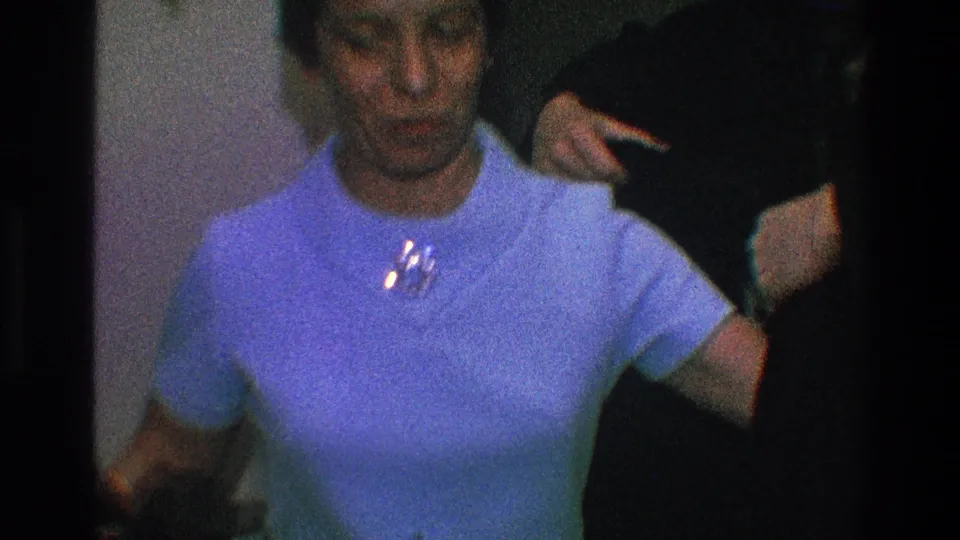 In 1968 Toledo home-movie footage, a woman in a light blue dress and brooch stands while someone helps position a dark coat behind her.