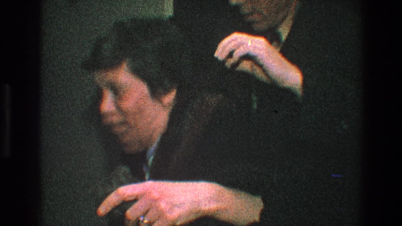 Man in a dark suit helps lift a dark coat near the woman's shoulder.