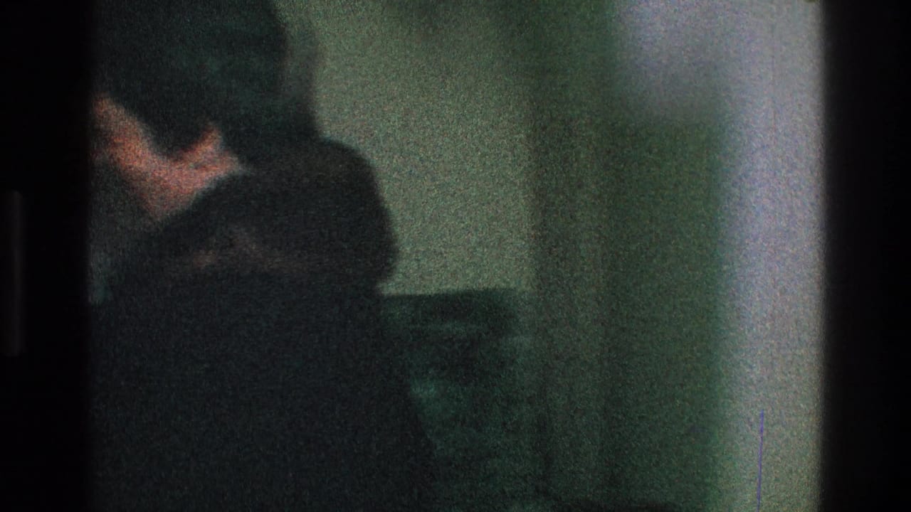 In a dim Toledo home interior from 1968, a partly visible adult in dark clothing appears near a wall and seating.
