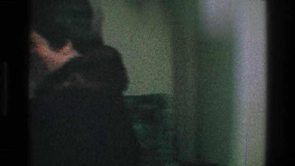In a dim Toledo home interior from 1968, a partly visible adult in dark clothing appears near a wall and seating.