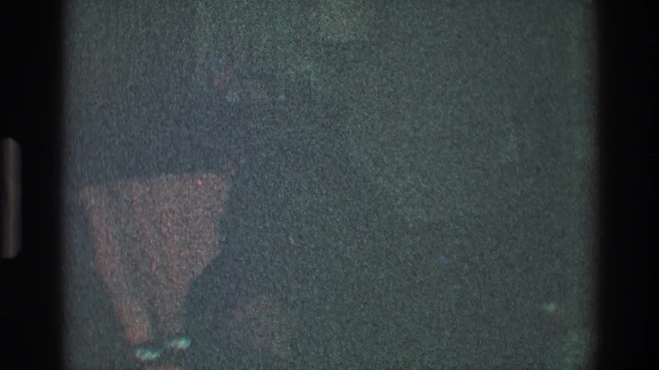 The 1968 Toledo home-movie frame shows a shadowed interior with a sofa or cushioned chair partly visible near the lower edge.