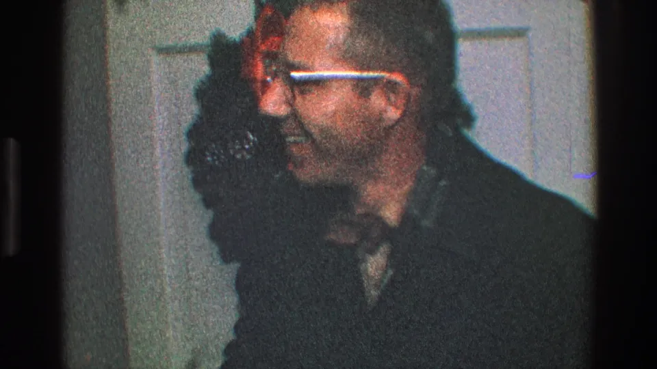 The man turns in profile, appearing to respond to someone off-camera near the Christmas wreath on the door.