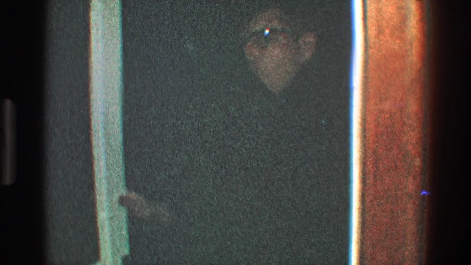 In 1968 Toledo home-movie footage, a man in glasses and a dark coat appears in a dim doorway with white trim.