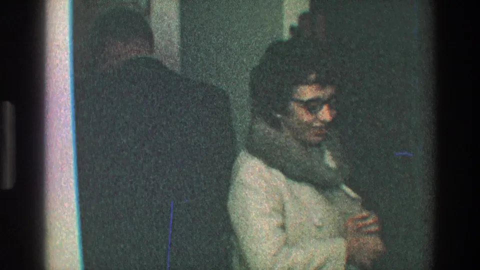 The woman faces the camera in a light coat with a fur hood, glasses, and pearl necklace inside a dim Toledo doorway scene from 1968.