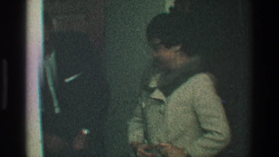 A side view shows the woman in a light coat with a fur hood near a man in a dark suit, both inside a dim private doorway scene.