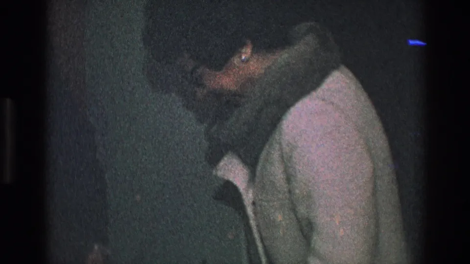 The man appears to lean in toward the woman in a light coat during the 1968 Toledo indoor home-movie scene.