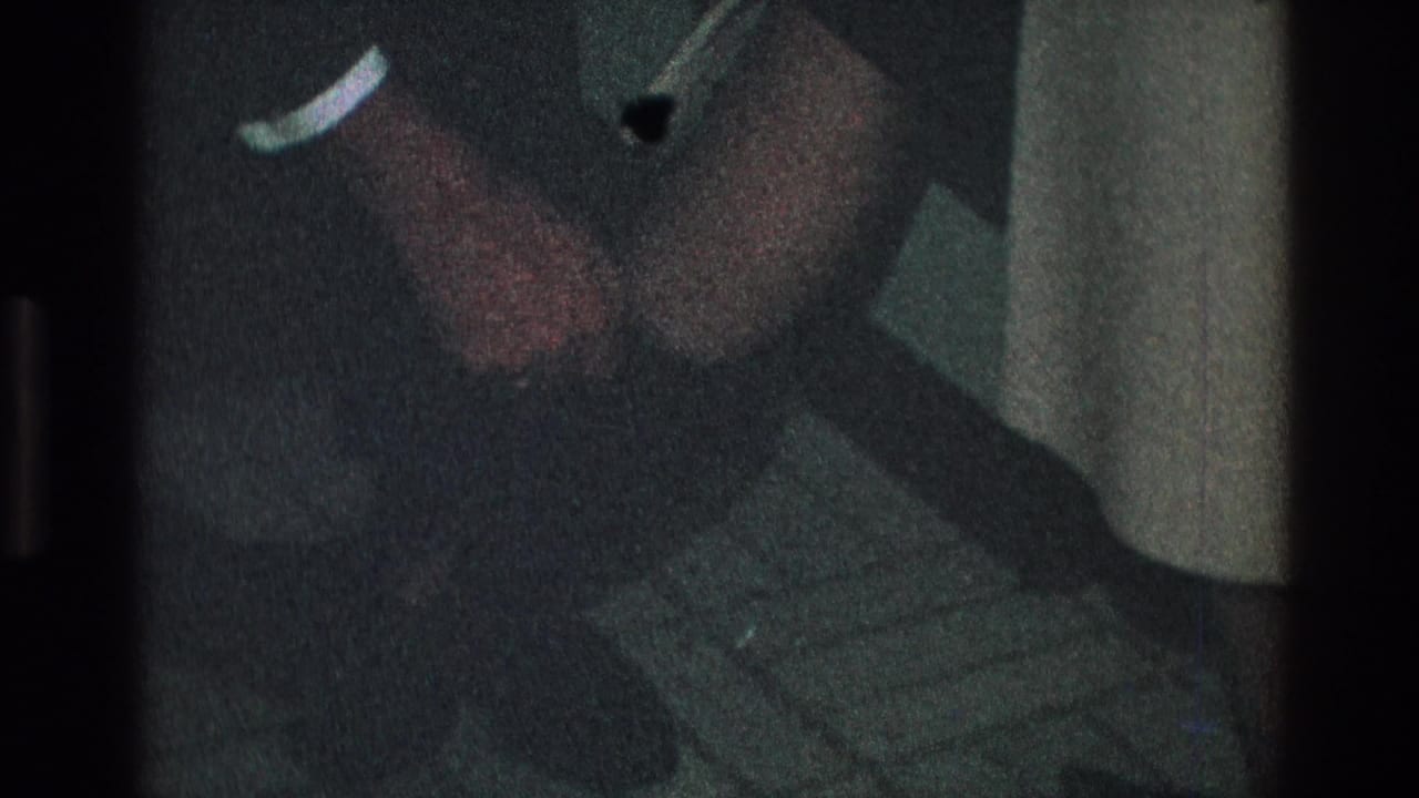 Toledo, Ohio 1968 home-movie frame showing a man in a dark sleeve and white cuff assisting near a woman's dark boot.
