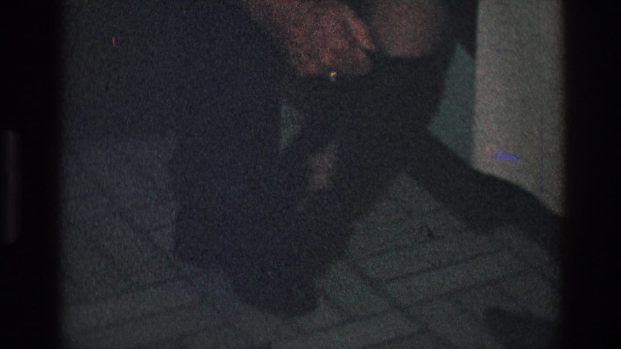 Man's hand rests near a woman's leg and dark boot on patterned tile.