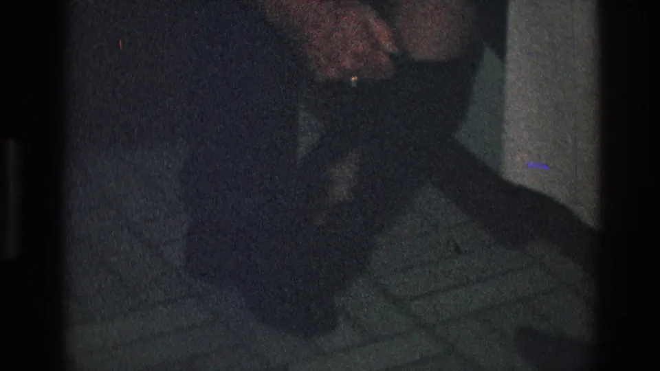 Toledo, Ohio 1968 frame with a close view of hands, a woman's leg, and dark footwear on a tiled surface.