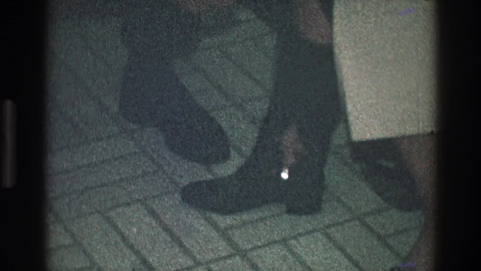 Final 1968 Toledo frame showing the woman's dark boot and lower leg on tile, with the assisting hand partly visible.