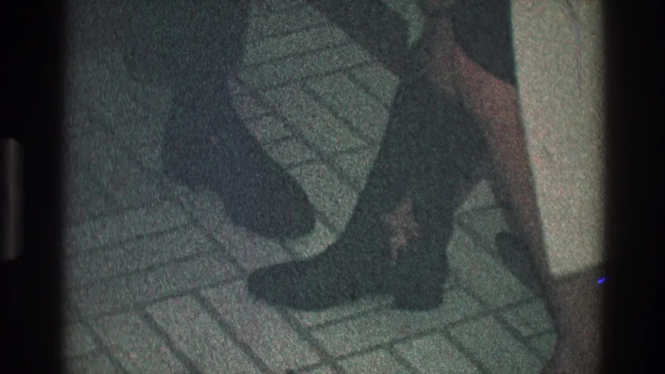 1968 Toledo home-movie frame showing dark leather boots, a short skirt, and patterned indoor tile flooring.