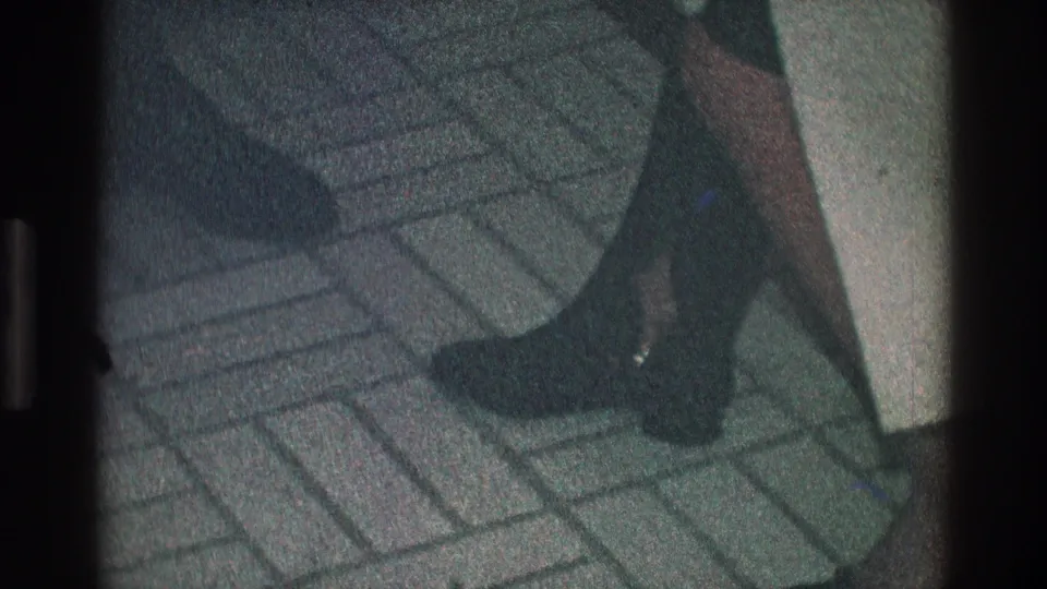Close 1968 Toledo home-movie view of dark boots, legs, and a short skirt on patterned tile flooring.