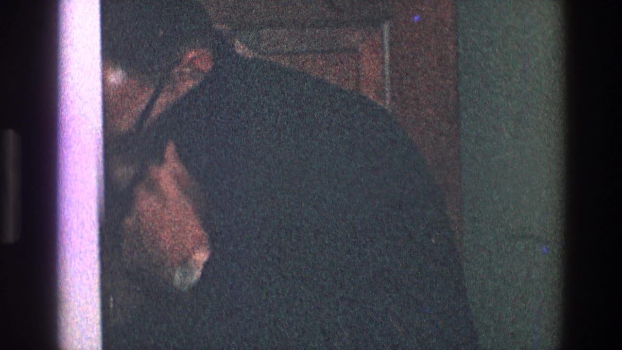 Man in a dark suit partly visible near a doorway in a dim interior.