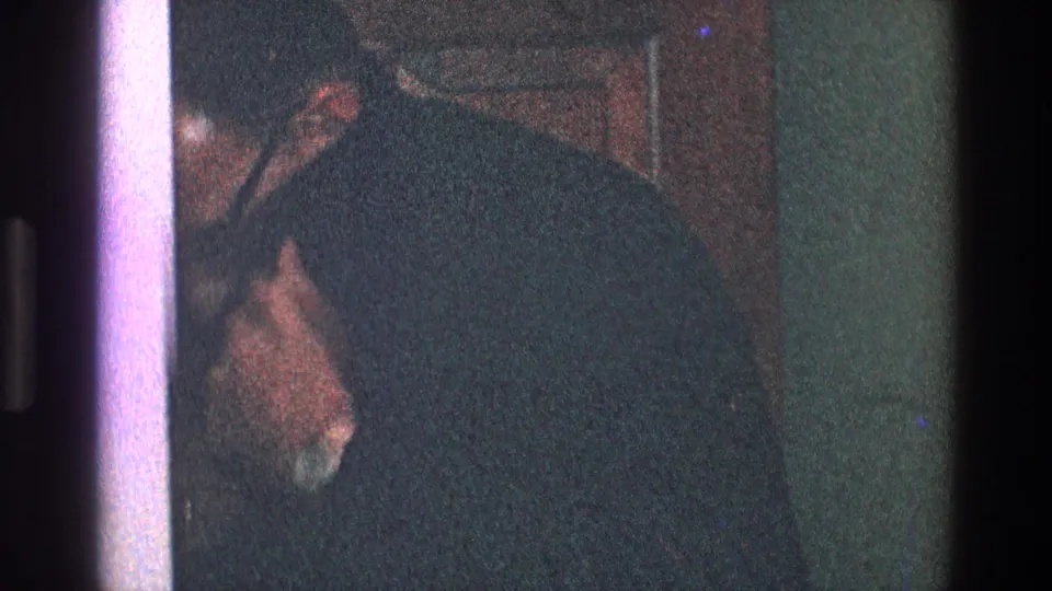 In 1968 Toledo home-movie footage, a suited man appears partly obscured near a door in a dim private interior.
