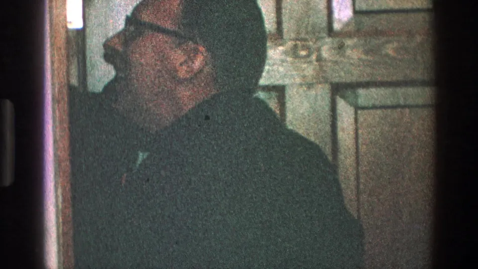 The 1968 Toledo frame shows a man in glasses in side profile against a wooden paneled door inside a private room.