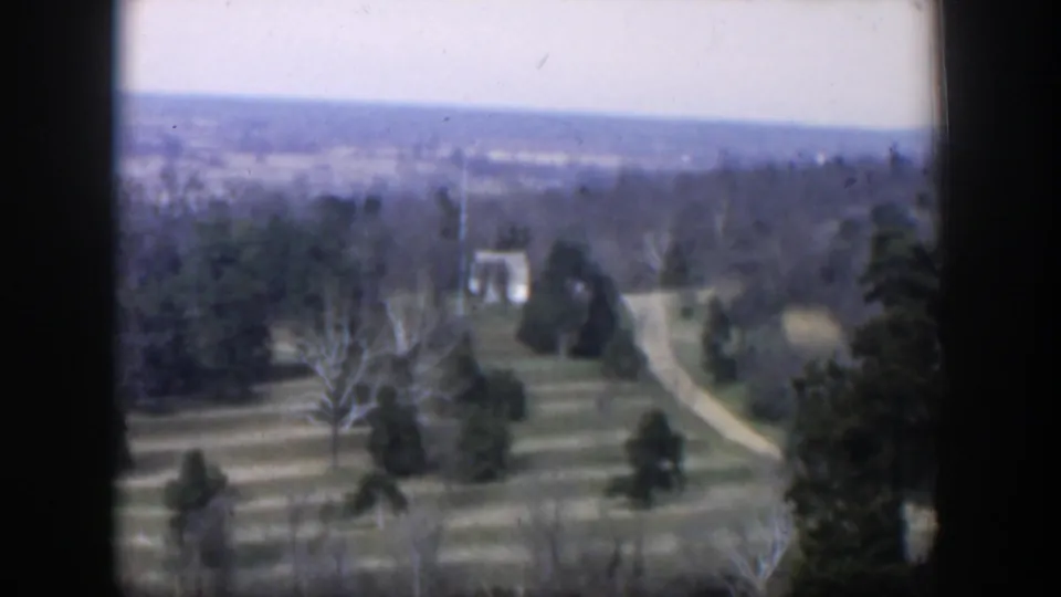 1951 Texas 8mm frame of winter terraced grounds, a winding dirt path, bare trees, evergreens, and a distant horizon.