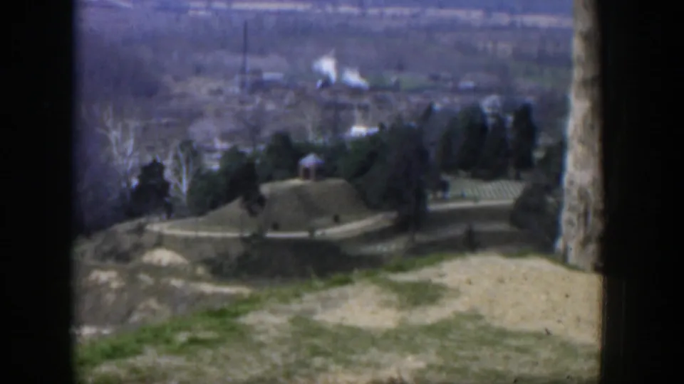 1951 Texas home-movie frame showing a hilltop foreground, winding road, small houses, trees, and hazy background terrain.