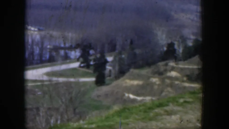 1951 Texas frame looking down from a hill toward a winding road, tree clusters, small structures, and hazy distant land.