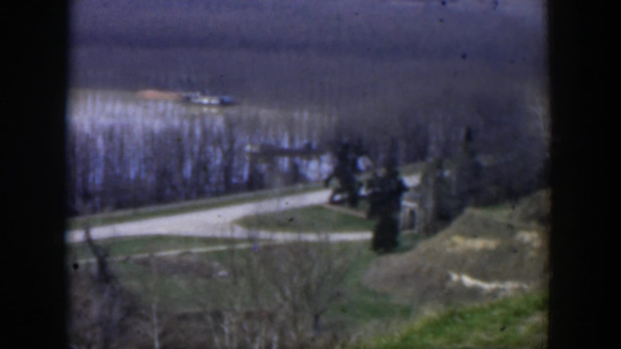 Elevated view of a curving road through open land with trees and a small structure near the edge.