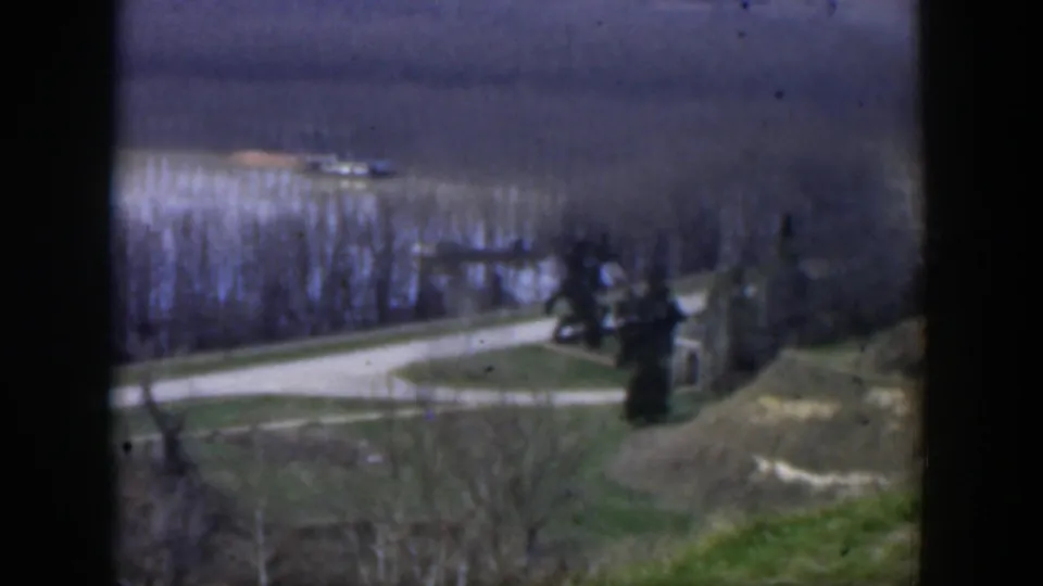 1951 Texas 8mm frame showing a curving road, open ground, sparse trees, and a small roadside structure from an elevated viewpoint.