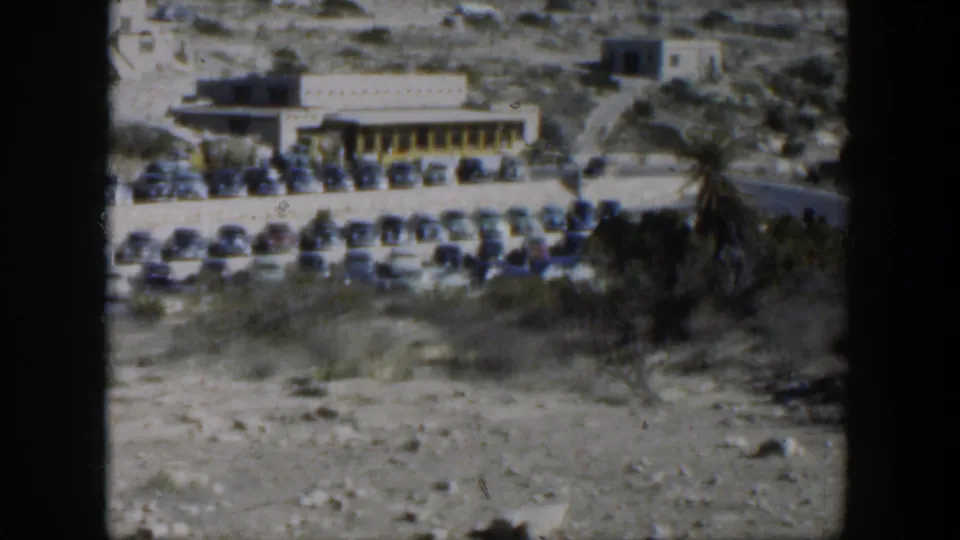 1951 Texas 8mm frame showing rows of classic cars parked by a low building in a dry roadside landscape.