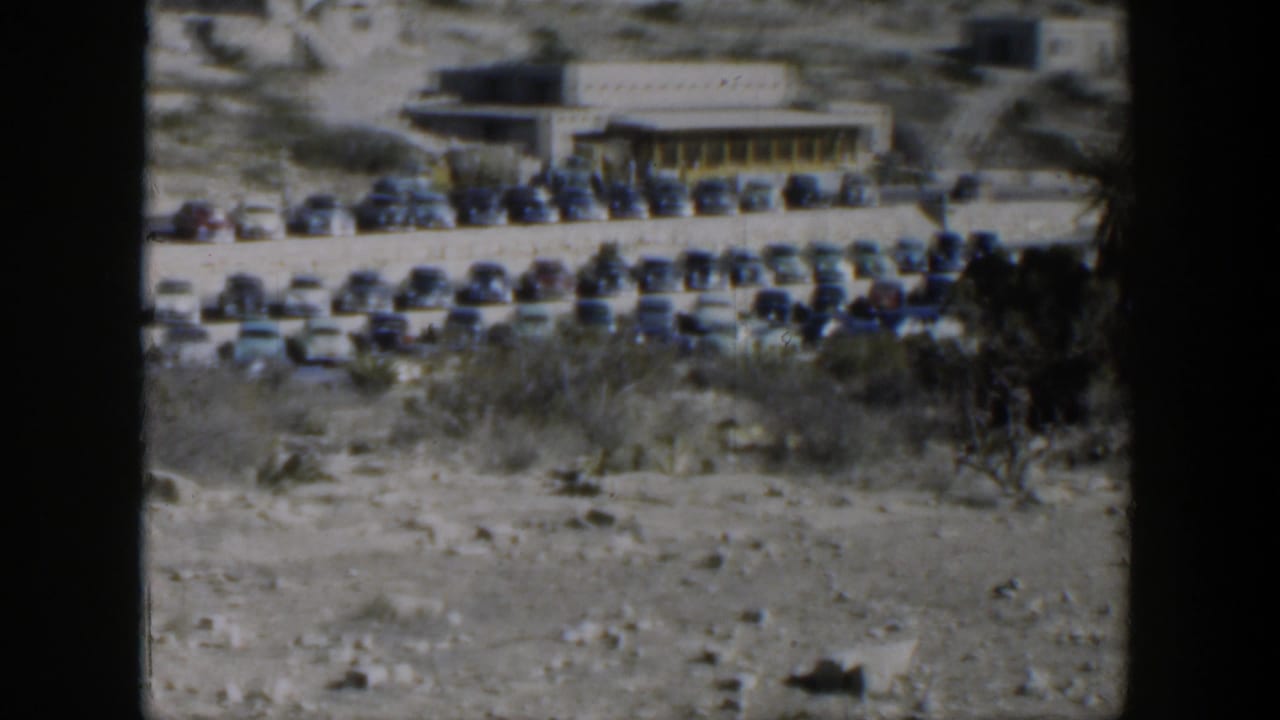 A 1951 Texas home-movie view of a roadside parking area with many cars and a low flat-roofed building.