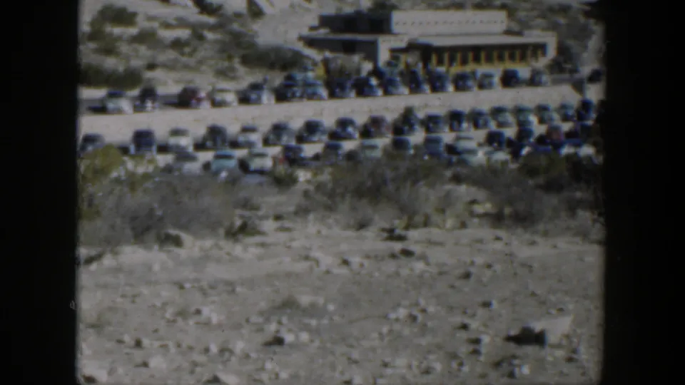 The 1951 Texas roadside scene continues with parked cars, desert vegetation, and a low building in the distance.