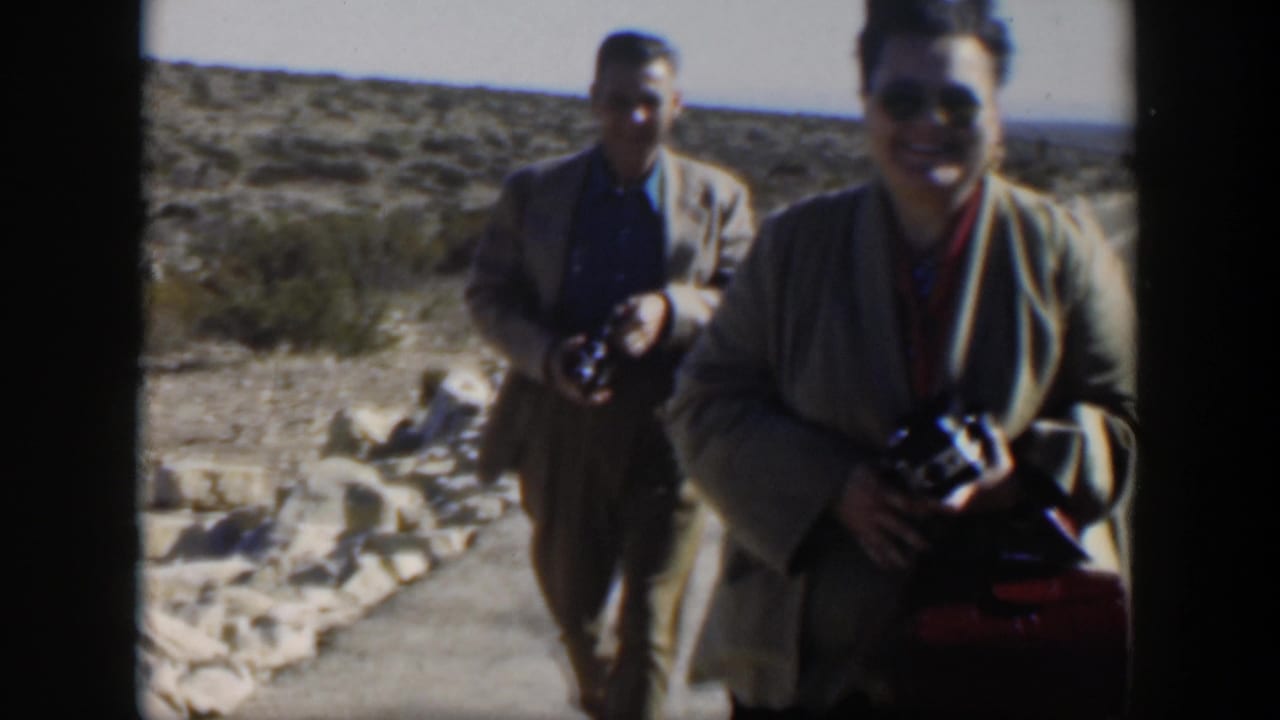 In 1951 Texas home-movie footage, two adults carrying cameras approach the viewer near a desert roadside or visitor area.