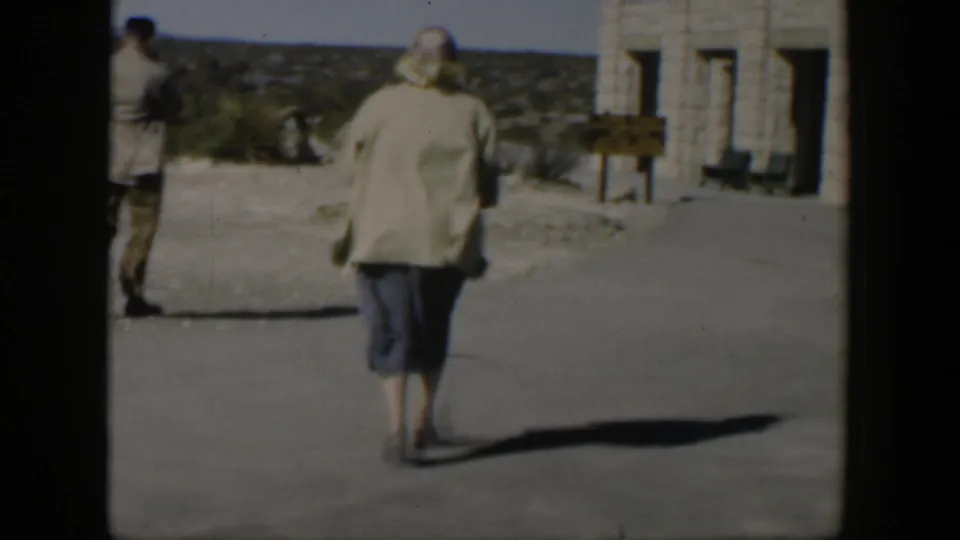 A woman in a light coat walks toward the stone building as another adult with a camera stands to the side in the 1951 Texas travel scene.