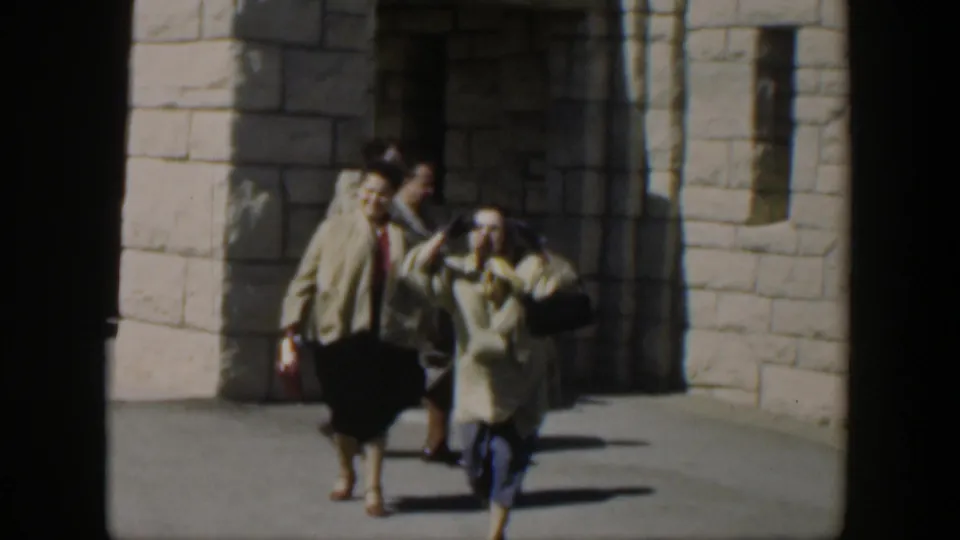 1951 Texas 8mm frame of women walking toward the camera in front of a pale stone doorway and wall.