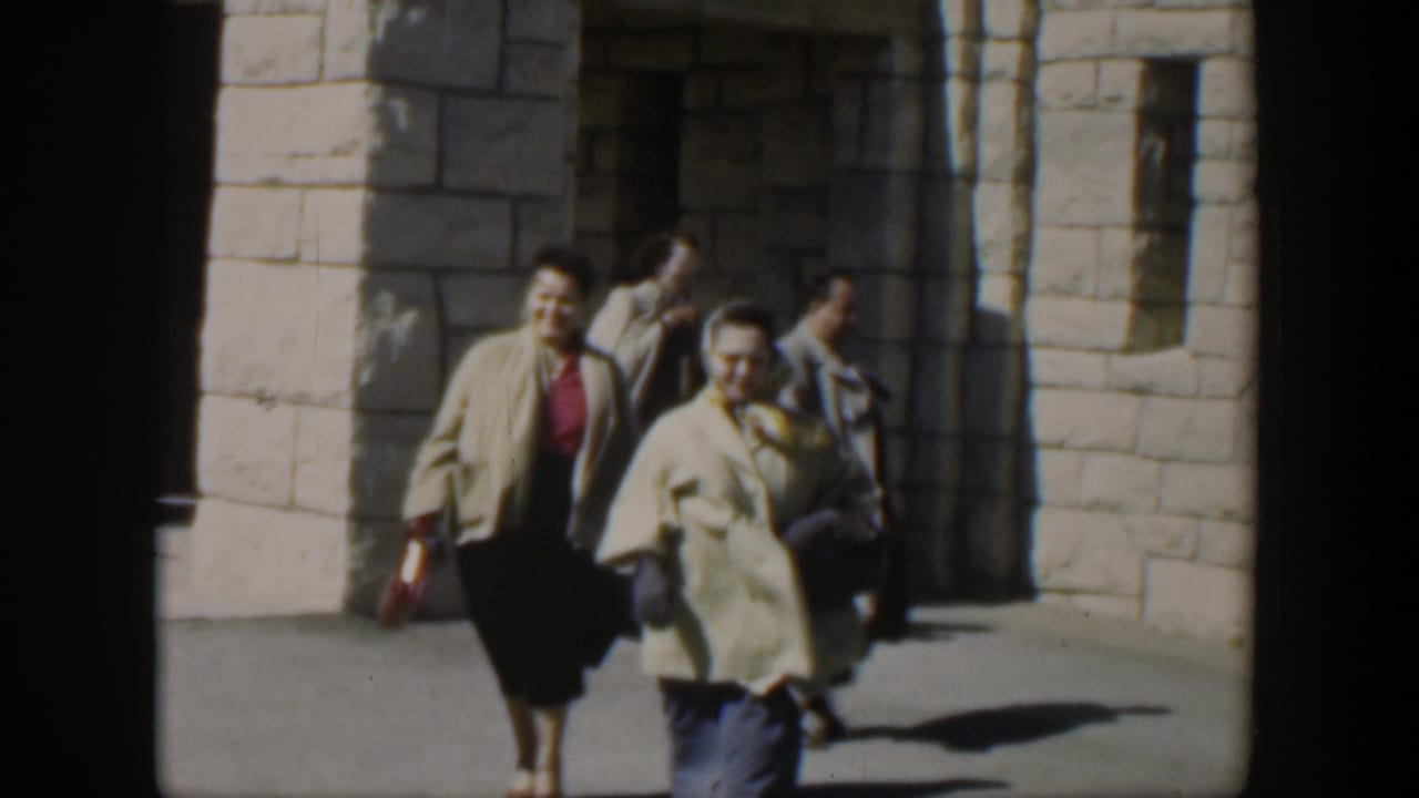 In 1951 Texas home-movie footage, two women in midcentury clothing walk past a white stone building with deep doorway shadows.