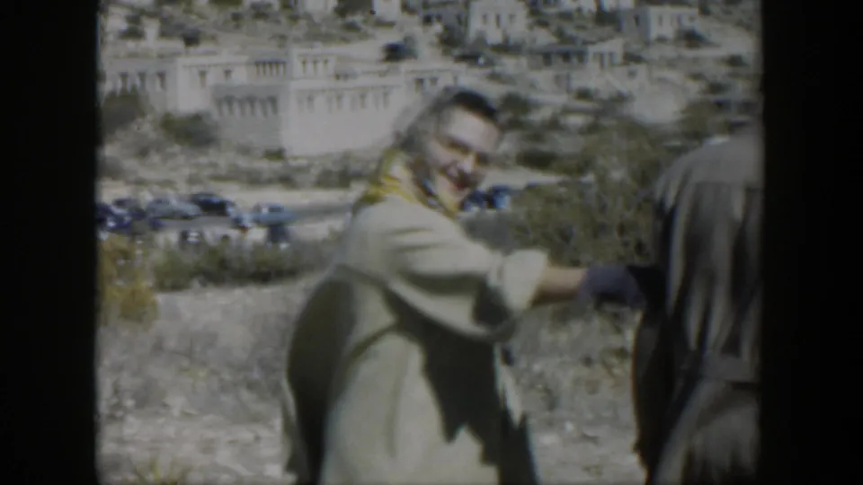 A smiling woman in a light coat and headscarf gestures beside a man during a 1951 Texas roadside home-movie moment.