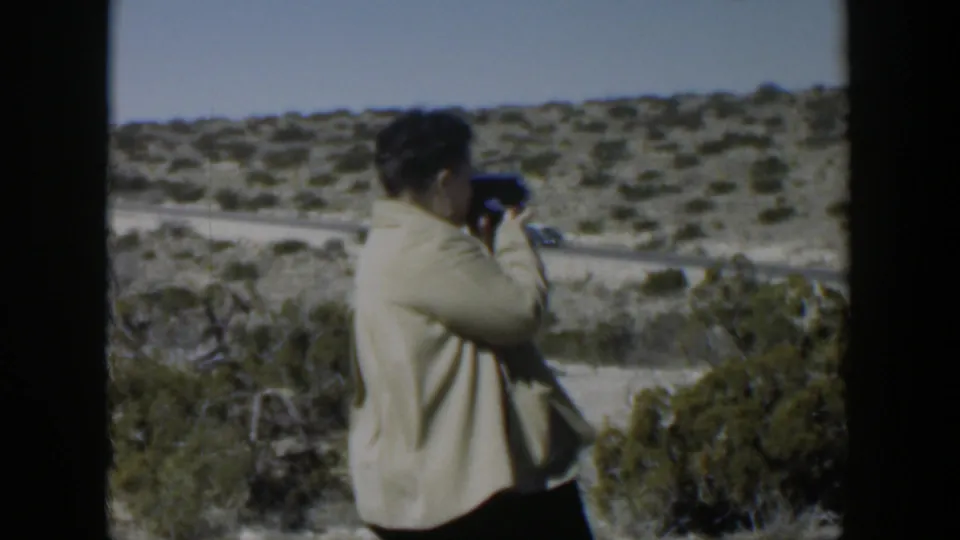 In 1951 Texas home-movie footage, a woman stands on arid ground filming a desert landscape and road with a small 8mm camera.