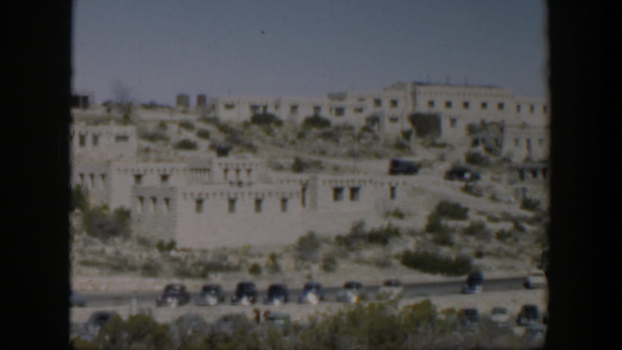 1951 Texas home-movie view of a pale hillside building complex above a road with mid-century cars.