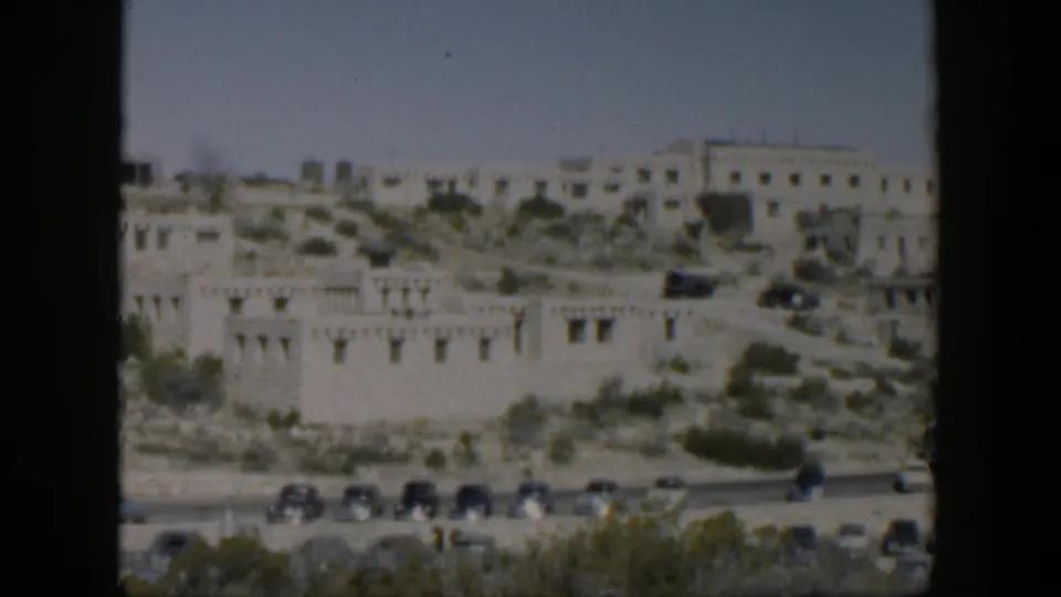 1951 Texas home-movie view of a pale hillside building complex above a road with mid-century cars.