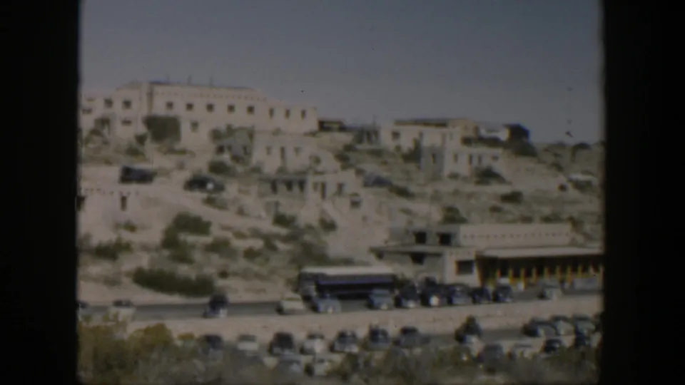 Texas 1951 exterior view of white hillside structures and sparse vegetation, with mid-century cars and a bus along the road below.