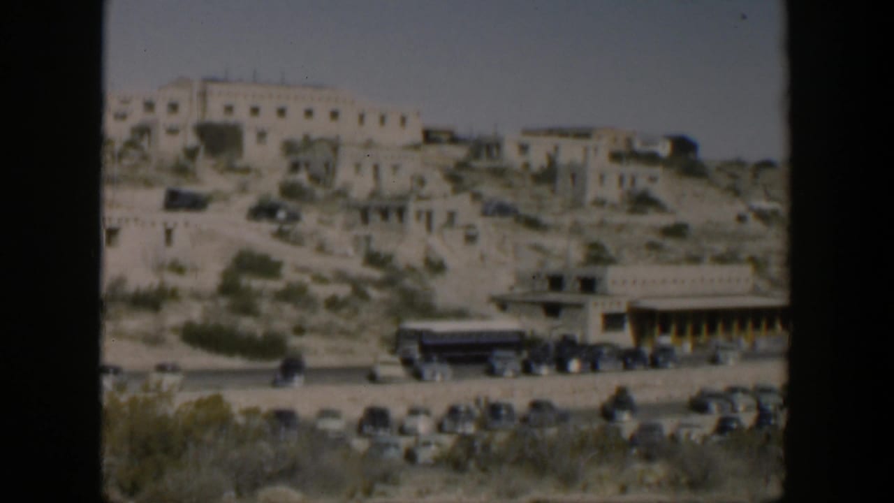 1951 Texas home-movie frame showing adobe-style hillside ruins above mid-century cars and a tour bus.