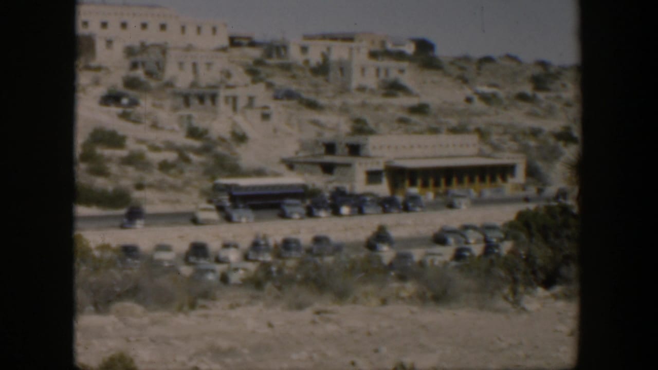 Wide 1951 Texas view of adobe-style hillside structures, roadside parking, and a tour bus below.