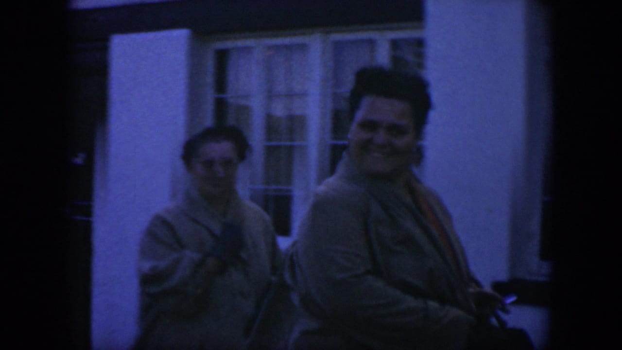 1951 Texas 8mm frame showing two adult women in sweaters walking outdoors beside a white building with white-framed windows.