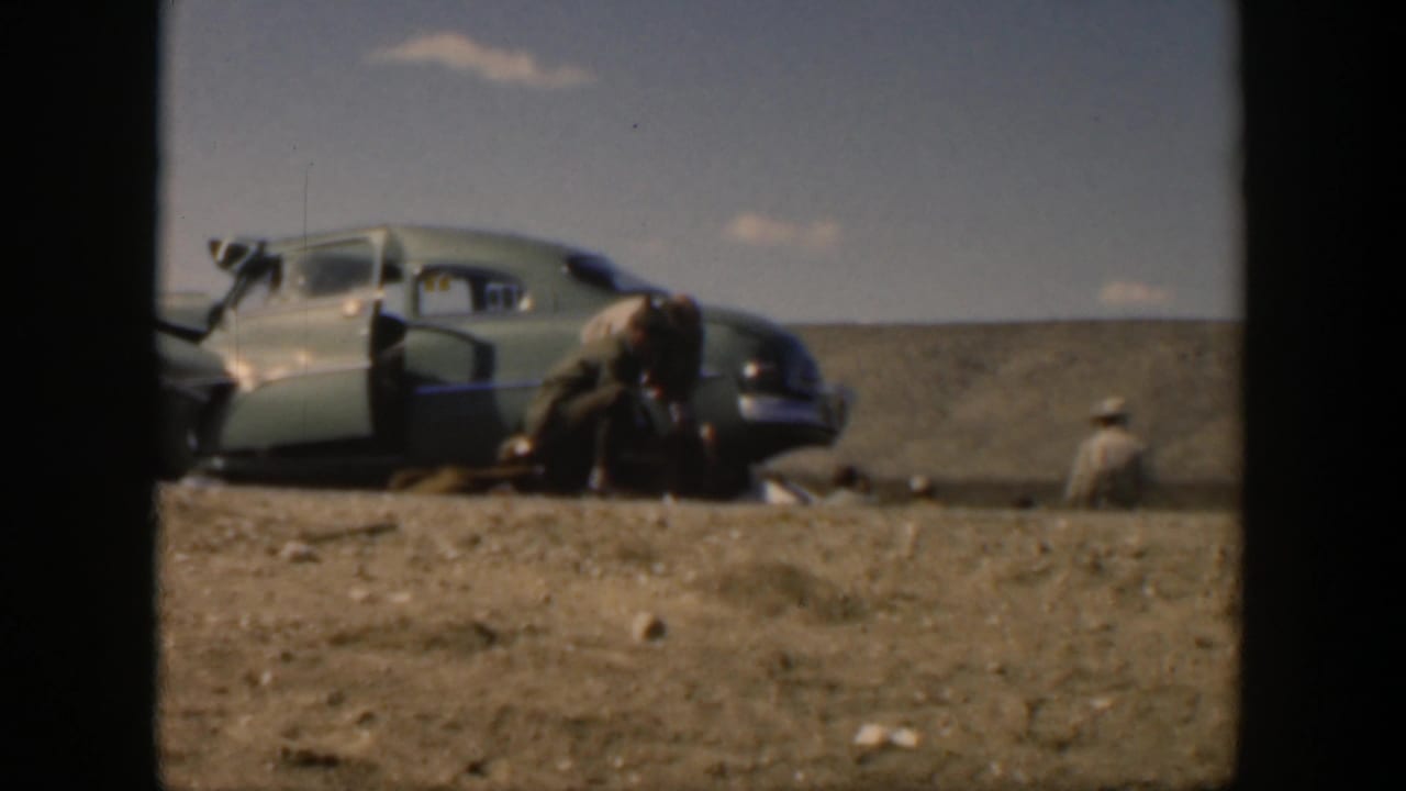 1951 Texas roadside accident frame with a soldier leaning toward an injured person beside a mid-century sedan.