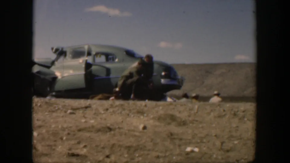1951 Texas 8mm frame showing roadside first aid beside a sedan in a sparse, dry landscape.