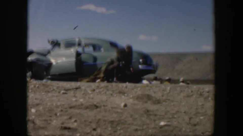 1951 Texas home-movie frame of soldiers assisting at a roadside automobile accident under a blue sky.