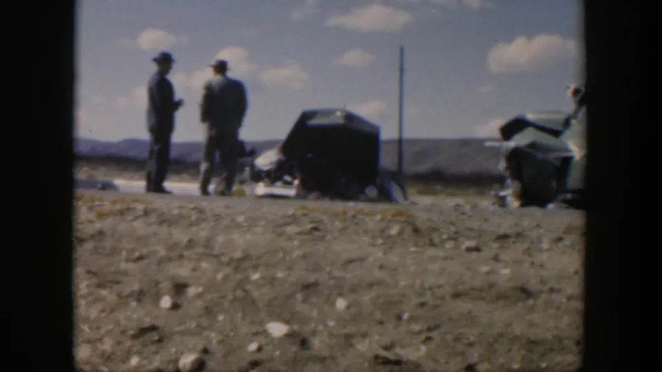 Texas 1951 8mm frame showing two men in hats standing near debris and a wrecked car on a dusty roadside.