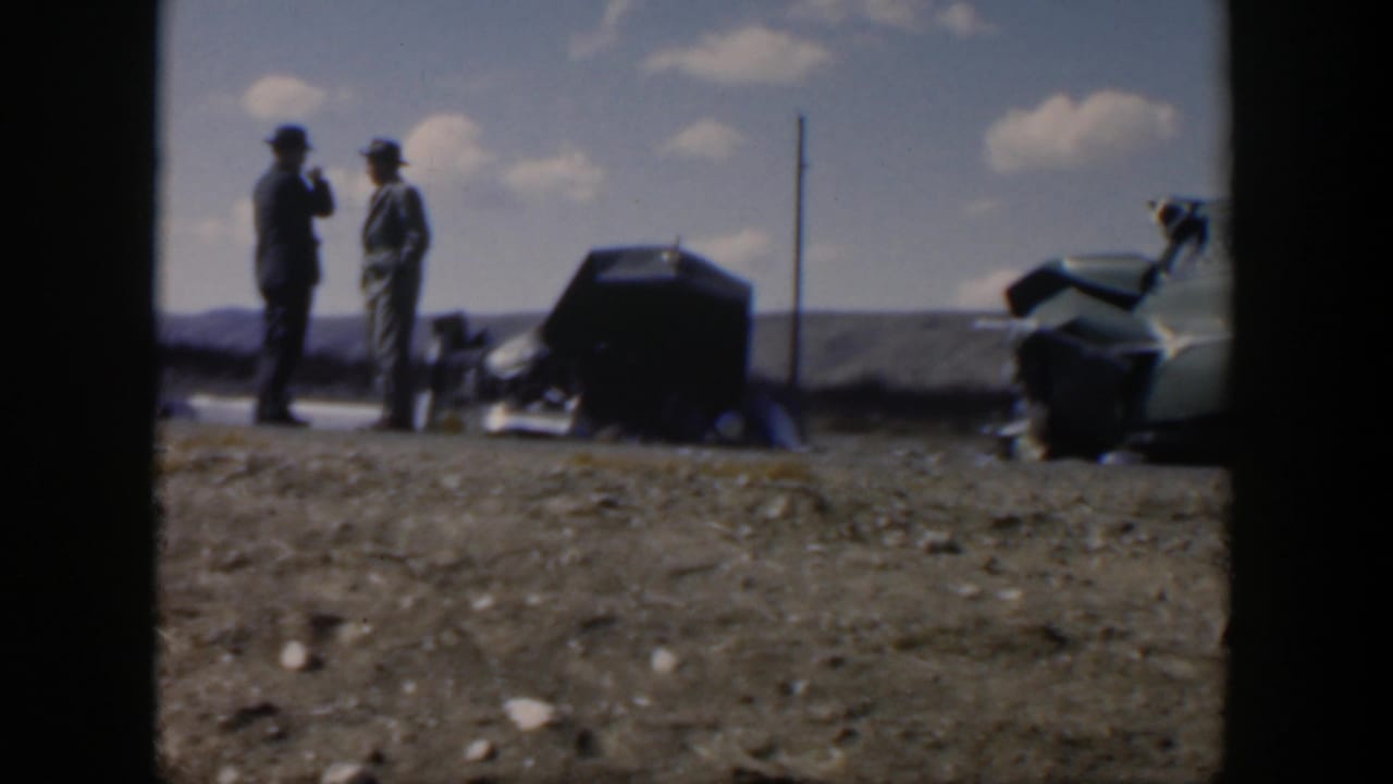 Two men stand near a roadside car with another vehicle shape partly visible at right.