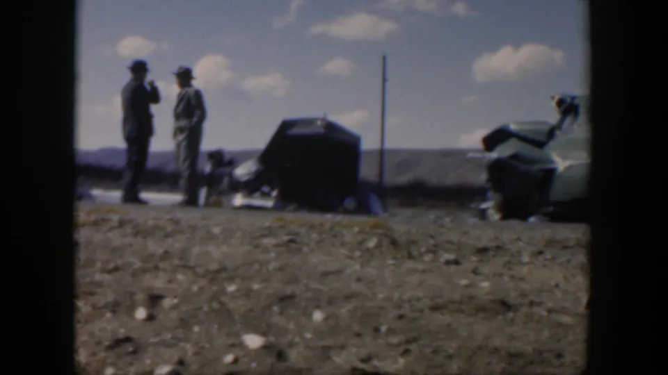 1951 Texas 8mm frame showing two men beside a roadside car on open ground, with another car area partly visible at right.
